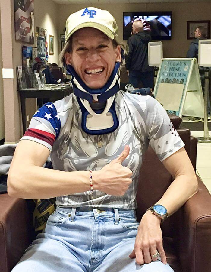 Abingdon Co. Image displaying ©2016 Retired Colonel Laurel “Buff” Burkel in her halo brace. woman sitting with a grey american pattern t shirt and blue jeans sitting down with her left arm up while having a thunbs up wearing a Bahama Blue Marina watch on her right wrist while she had a neck brace smiling.