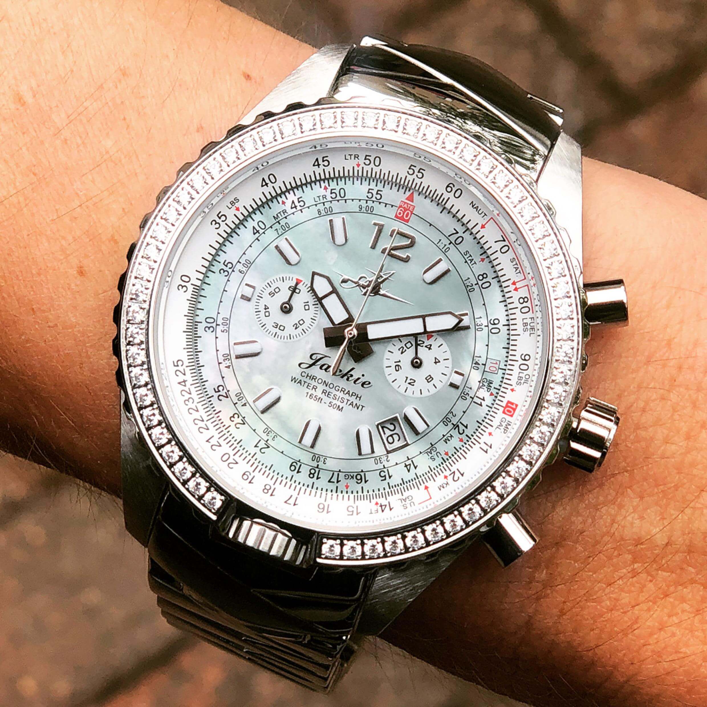 Abingdon Co. Image displays Jackie aviation pilot watch in seaplane green with swarovski crystals or diamonds around the case on a woman's wrist with a brick background. Jackie aviator's watch will do all pilot calculations and display date, military time, and have 60 min stopwatch