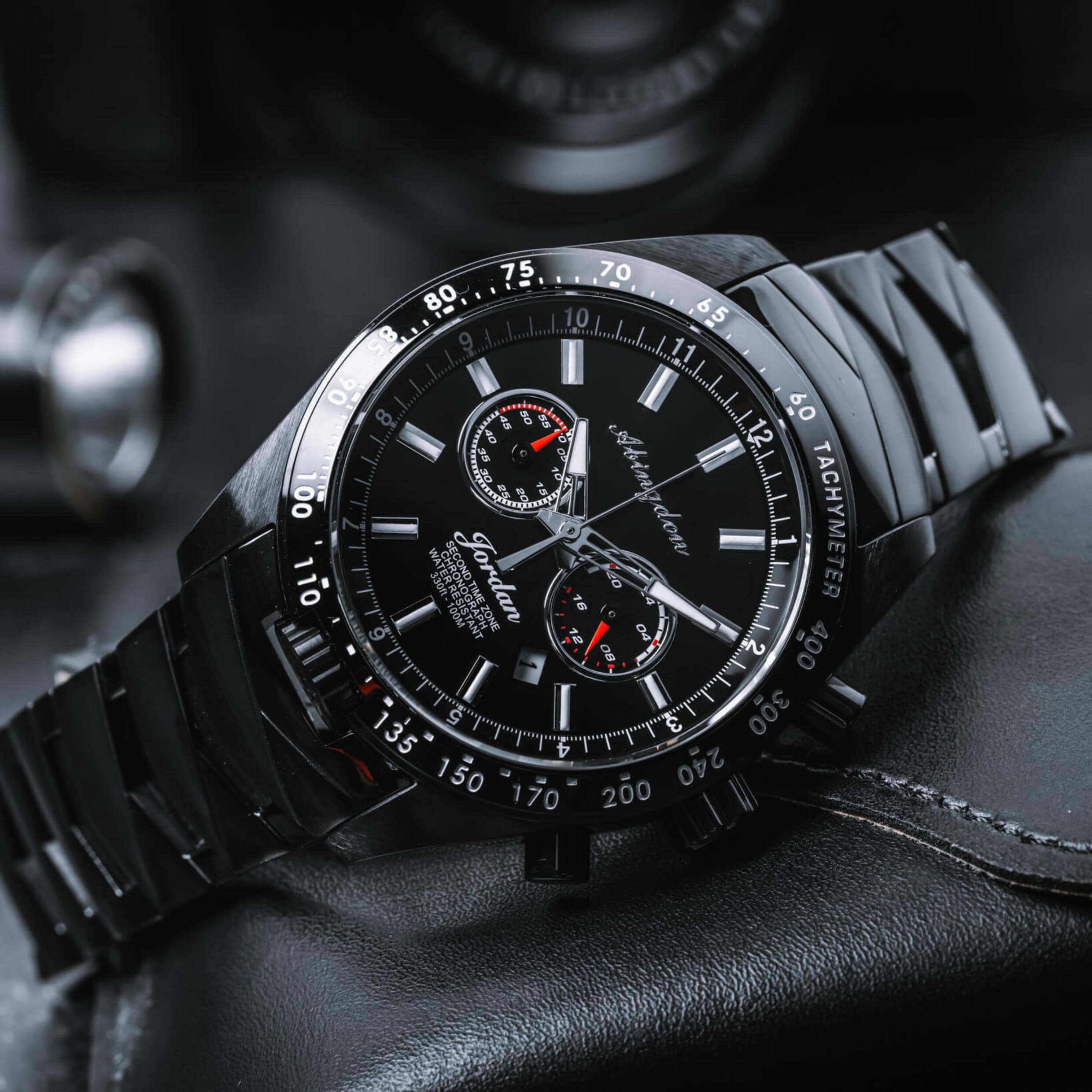Abingdon Co. Image displays Jordan watch on a black background. black chronograph watch with tachymeter, military time, date, and glow in the dark markings. Automotive unisex style watch with red accent markings on the black sunray dial. Racing watch for men and women.