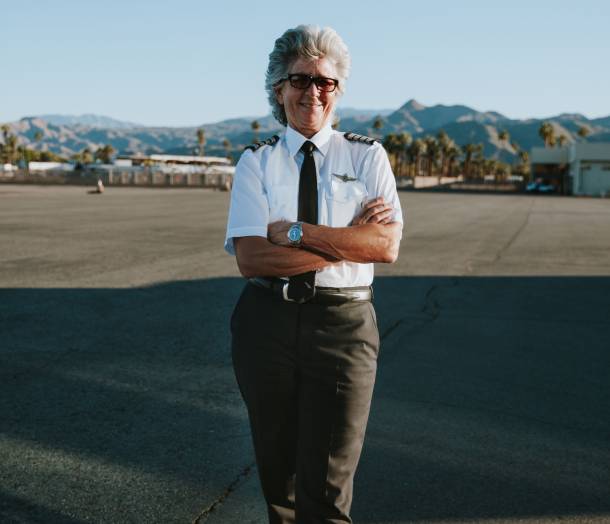 Captain Jan Anderson outside at the airport standing with her arms crossed in her pilot's uniform looking into the camera.