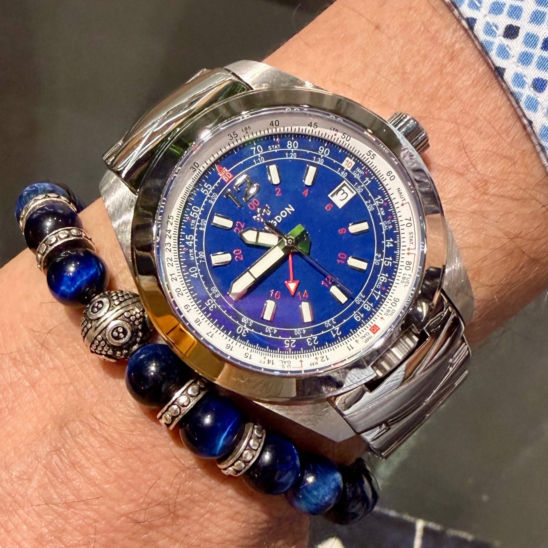 Abingdon Co. image displaying Bonneville Blue silver steel analog watch with steel strap on a wrist with a blue and silver bracelet. Blue dial with Red GMT and E6B flight computer. Sapphire crystal, Swiss movement. Limited Edition 18 pieces only