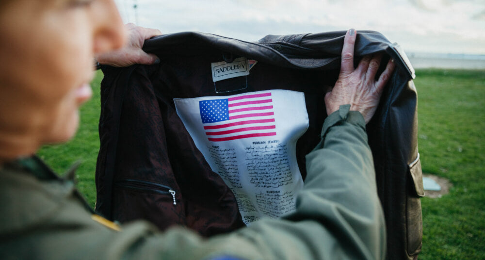 Abingdon Co image of a woman holding a dark leather jacket with an American flag design on a grassy field