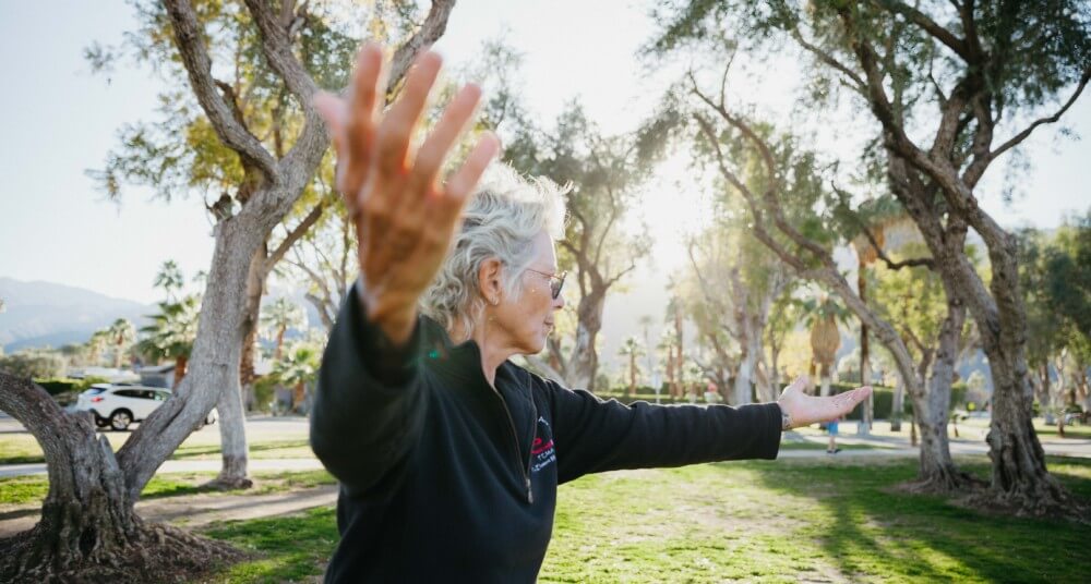 Abingdon Co. Image displaying ©2023 martial artist, Kore Grate, an older woman with short white hair, demonstrating martial arts in a park in her black gi