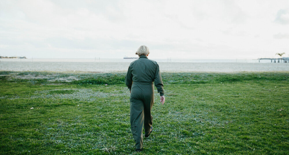 Abingdon Co image of a woman walking away from the camera on a grassy field with a distant view of water and sky.