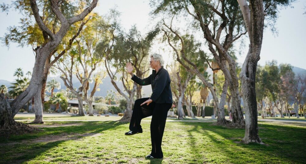 Martial artist, Kore Grate, an older woman with short white hair, demonstrating martial arts in a park in her black gi