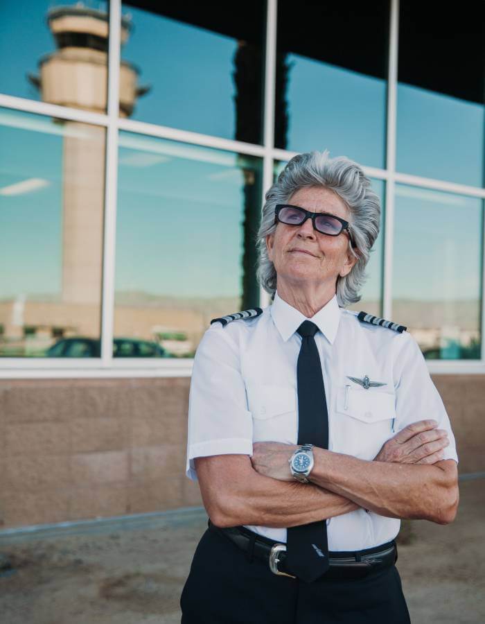 Abingdon Co. Image displays Captain Jan Anderson is ready to fly. An older woman in a pilot uniform with her arms cross looking towards the sky smirking while she wears an Abingdon watch