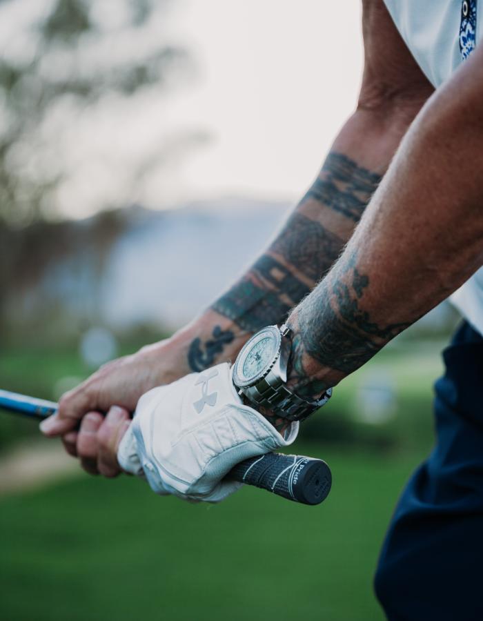 Abingdon Co. Image displaying ©2022 Black Belt and Tattoo Artist, Koré Grate's tattooed arms holding a golf club on the course in mid swing.