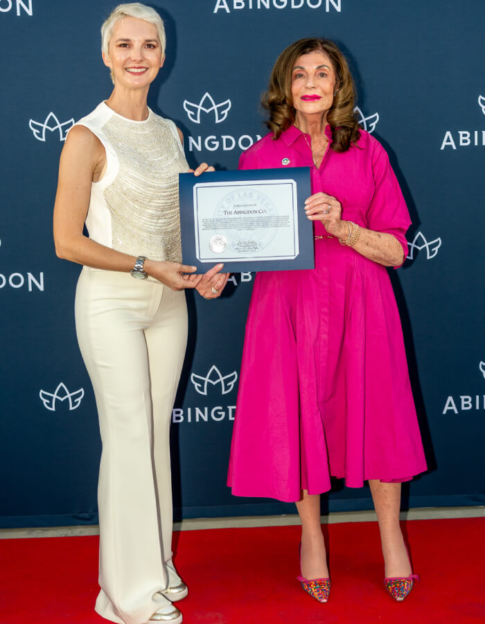 Two women, Abingdon Mullin and Mayor Shelley Berkley, on a red carpet holding an award in front of an Abingdon backdrop