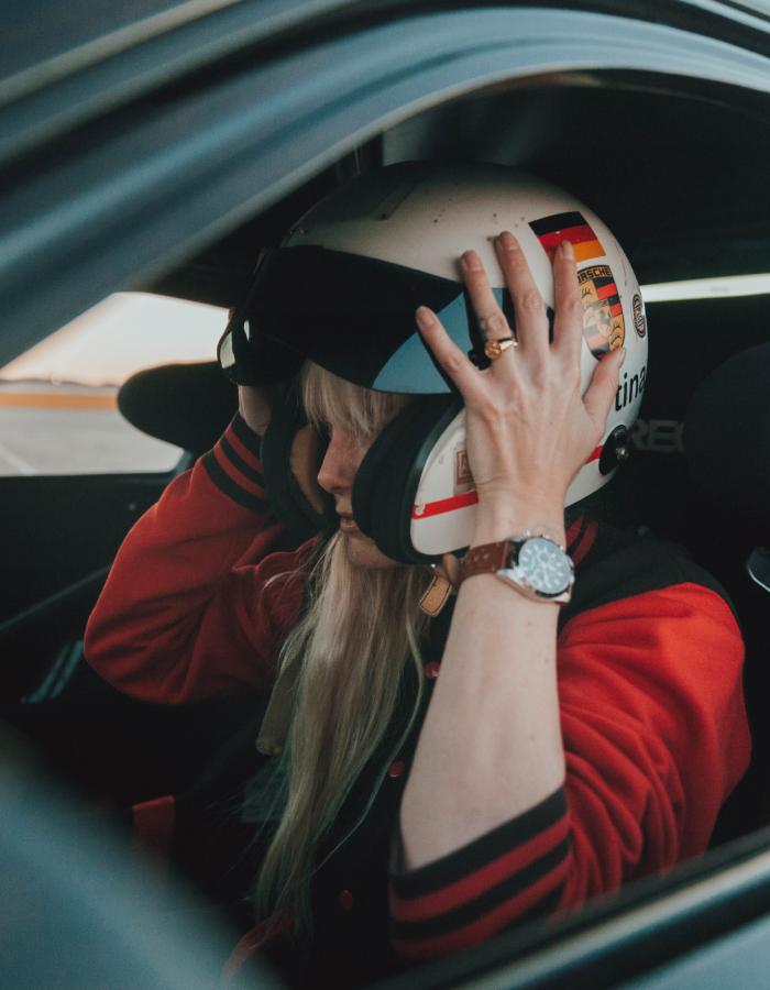 Abingdon Co. Image Displays Model actress, Eugenia Kuzmina sitting in a race car with her hands lifting a helmet to her head while she wearing a red and black jacket