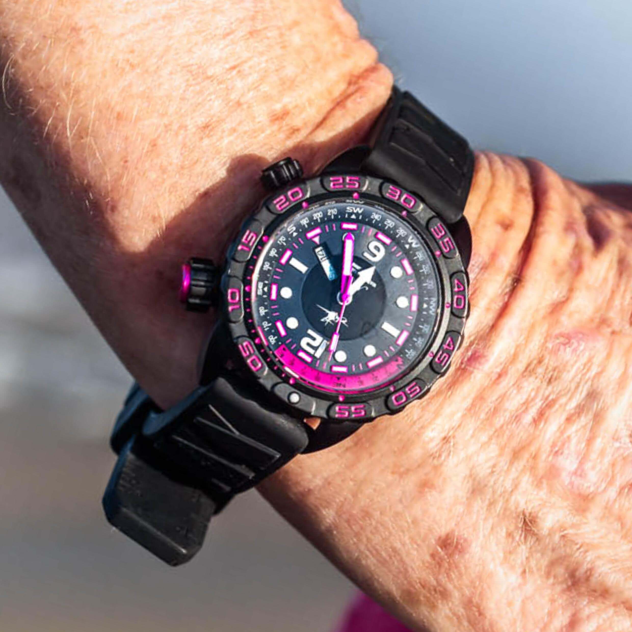 Abingdon Co. Image displays Nadia dive watch on woman's wrist outside in the sun at the beach. Black women's dive watch with hot pink accents.