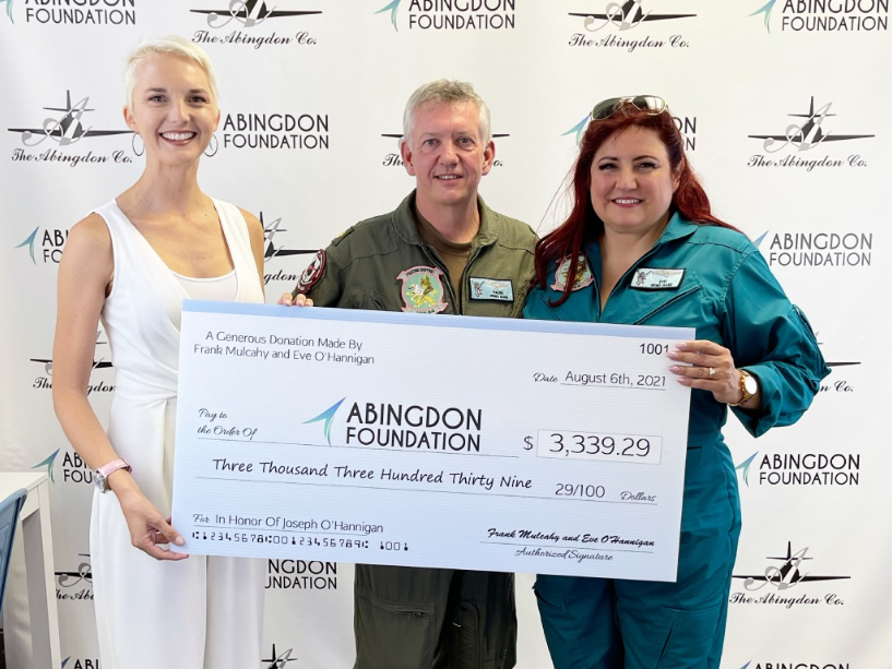 Abingdon Co. A image displaying Abingdon is presented with a big check award for the foundation by a couple against a stop and repeat. All three adults are standing and posing for the camera with smiles.